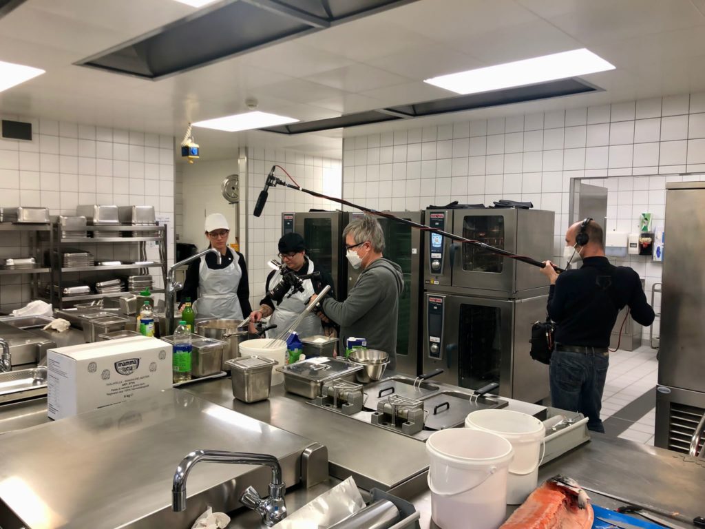 Ein Filmteam filmt in der Küche bei der Essensvorbereitung am BFW Düren. Eine Ausbilderin ist mit ihrer Auszubildenden zur Fachpraktikerin Küche zu sehen.